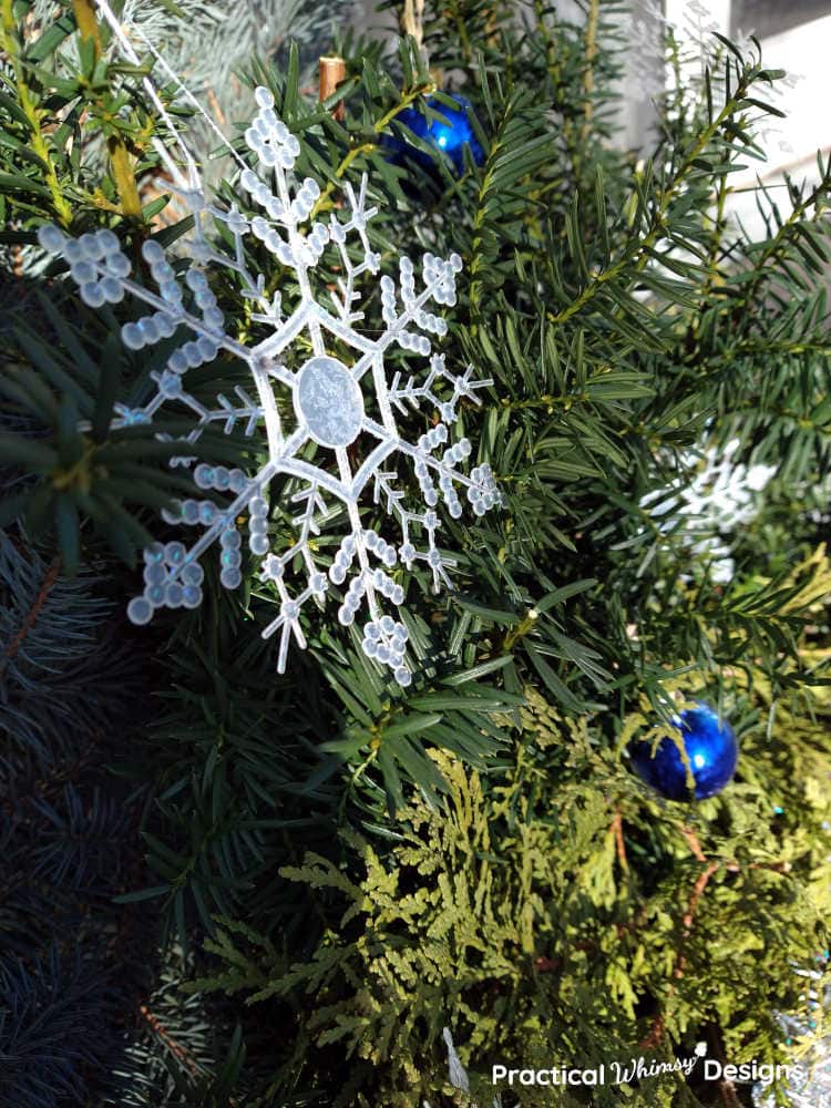 Snowflakes and blue ornaments hanging from evergreens on porch pot
