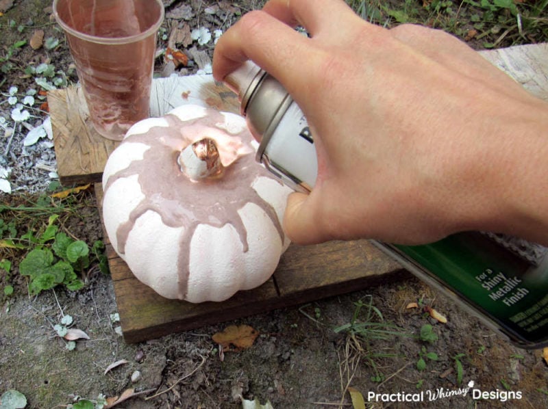 Spraying copper paint on top of foam pumpkin and glue.