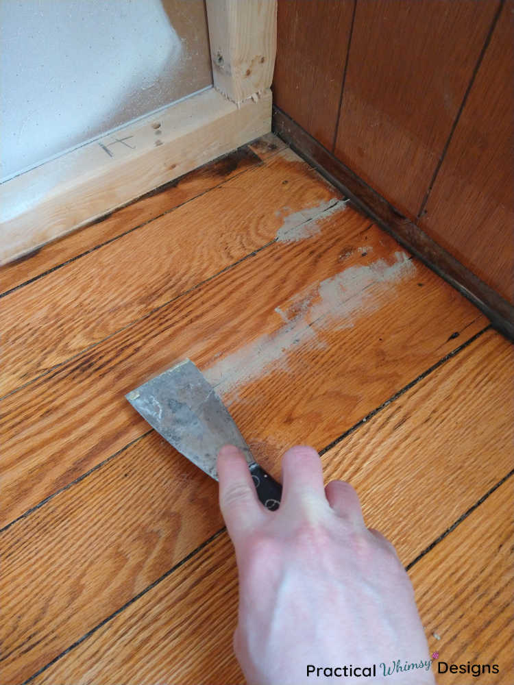 Working wood filler into gaps in the hardwood floors with a putty knife.