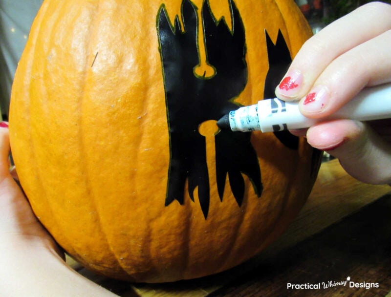 Tracing boo stencil onto pumpkin with a marker