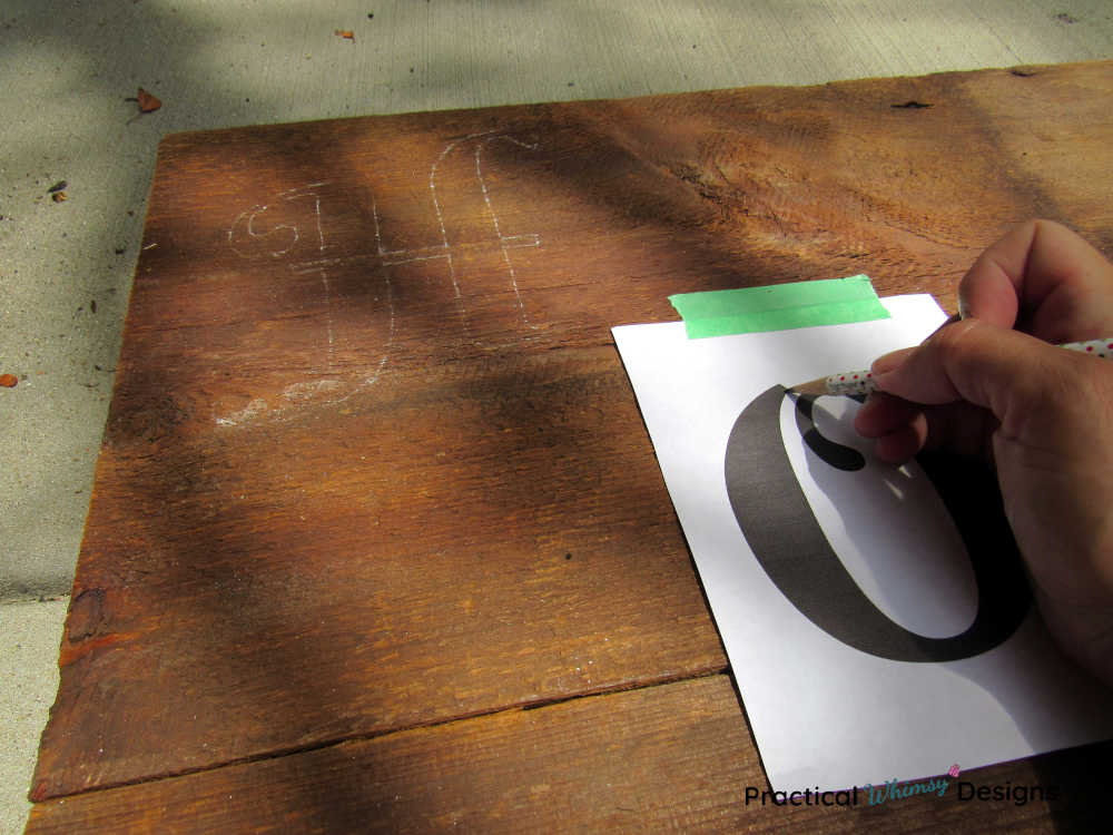 Hand tracing letters onto a wooden sign.