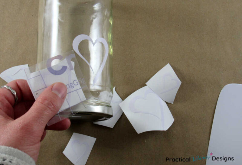 Applying vinyl hearts on glass jar with transfer tape.