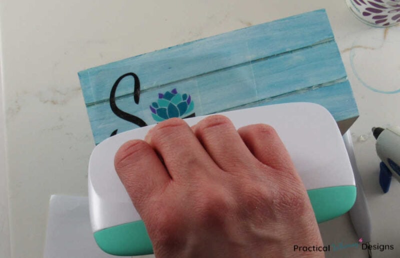 Using a plastic scraper to adhere vinyl to a wooden crate