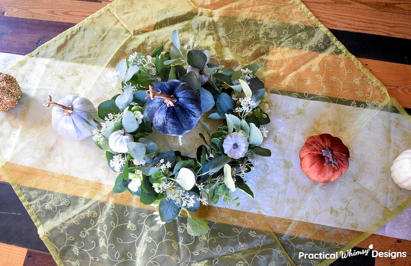 Velvet pumpkins and green wreath centerpiece on white and green cloth in dinning room.