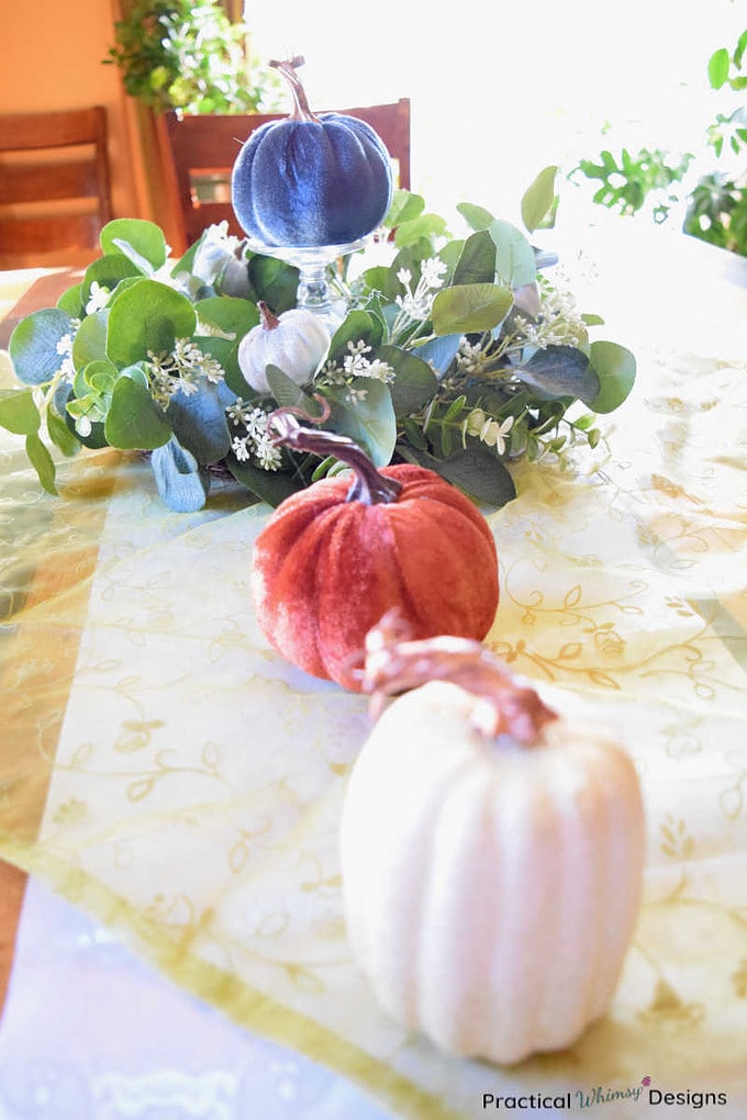 White, orange, and blue pumpkins with wreath on dinning room table.