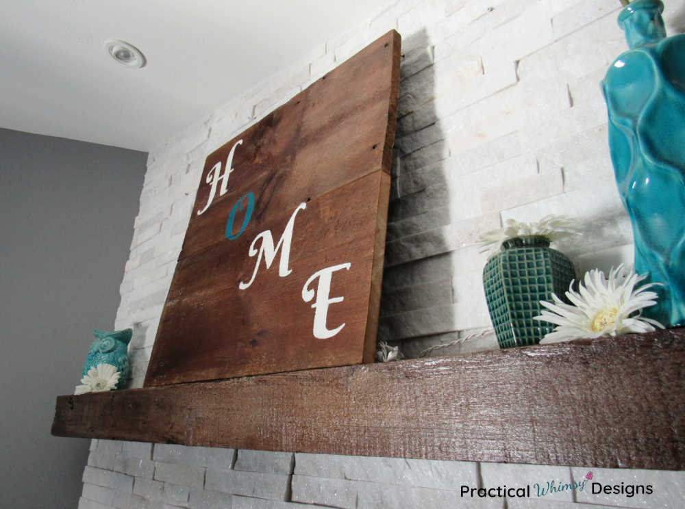 Wooden home sign on mantel with teal vases, white flowers, and teal owl