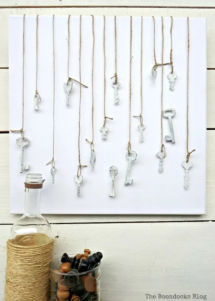 Painted keys hanging from string on blank canvas.