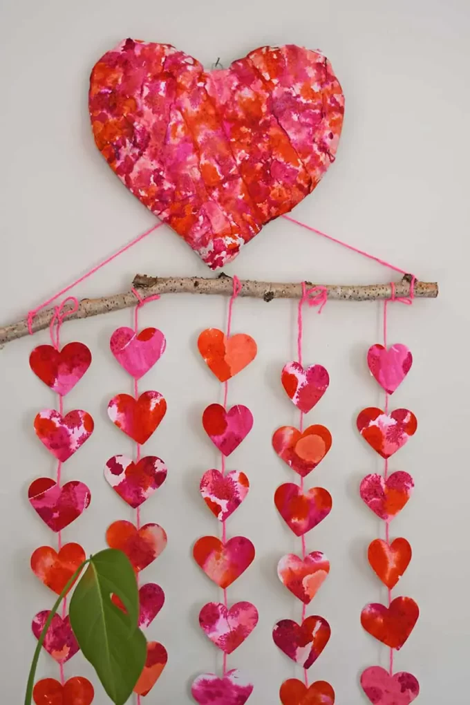 Red and pink large paper mache heart with watercolor hearts hanging below on a stick.