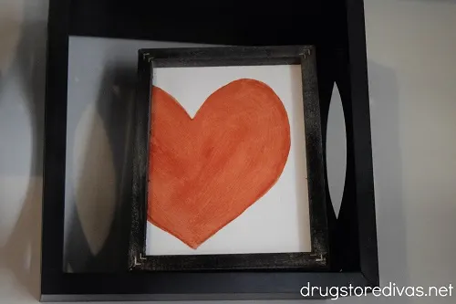 Red heart reverse canvas art with black frame.
