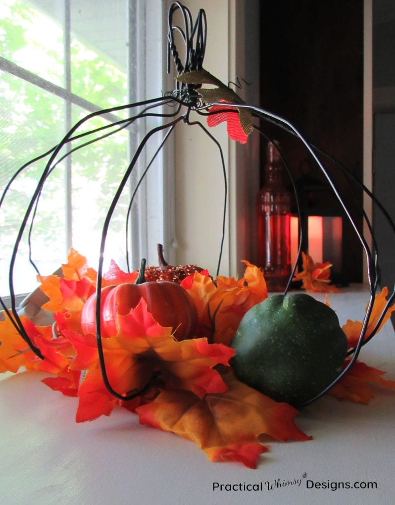 Using pumpkins in easy indoor fall decorations: wire pumpkin with leaves and small pumpkins inside.